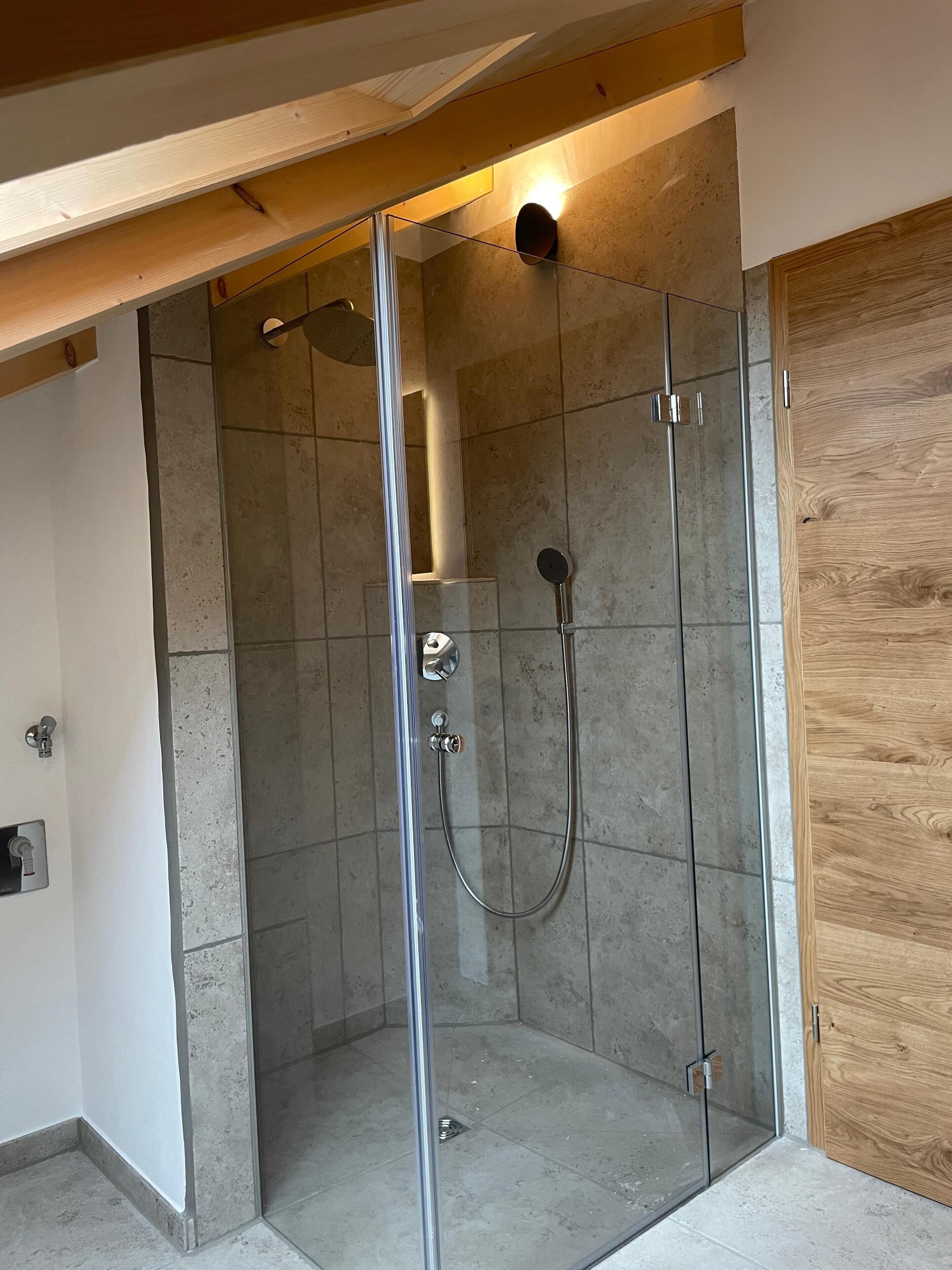 Une douche fermée par des parois en verre, dotée d’un pommeau de douche à main et d’un robinet fixé au mur.