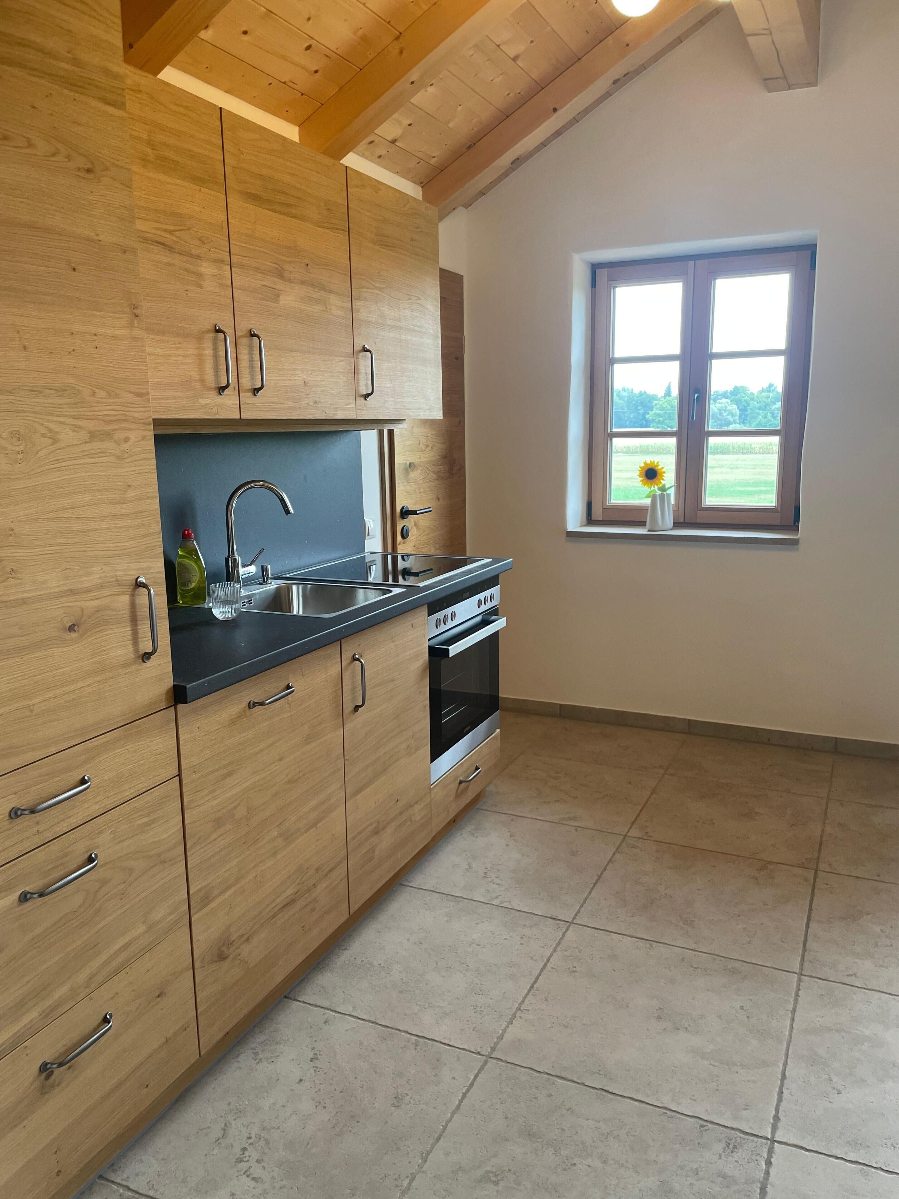 A kitchen with wooden cabinets, a stainless steel sink, and a window with a view of greenery.