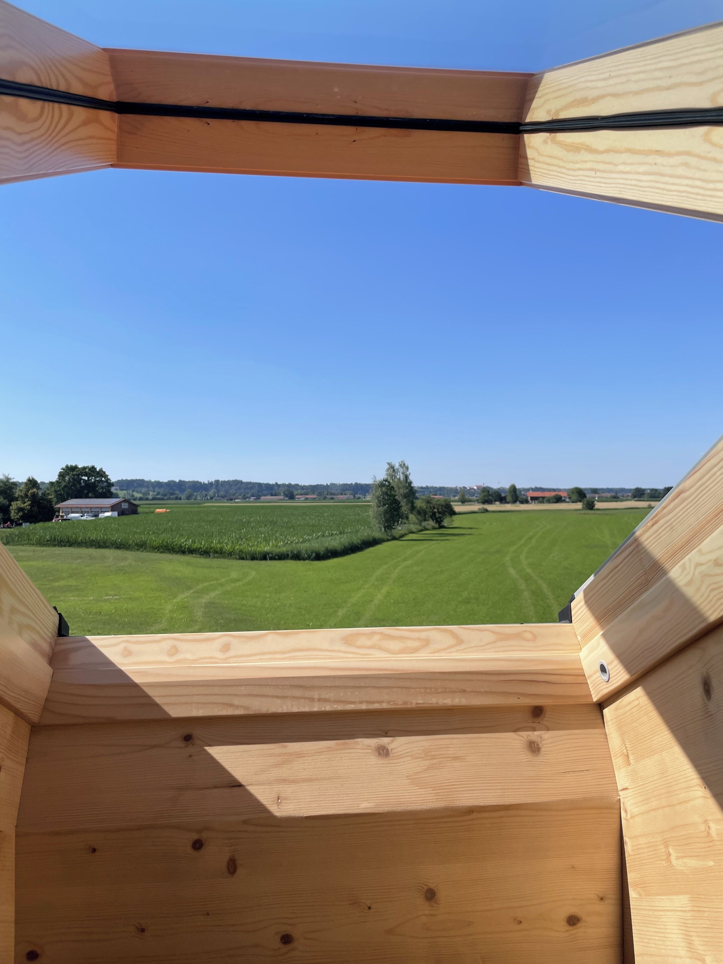 A wooden structure with a view of a green field and distant buildings.