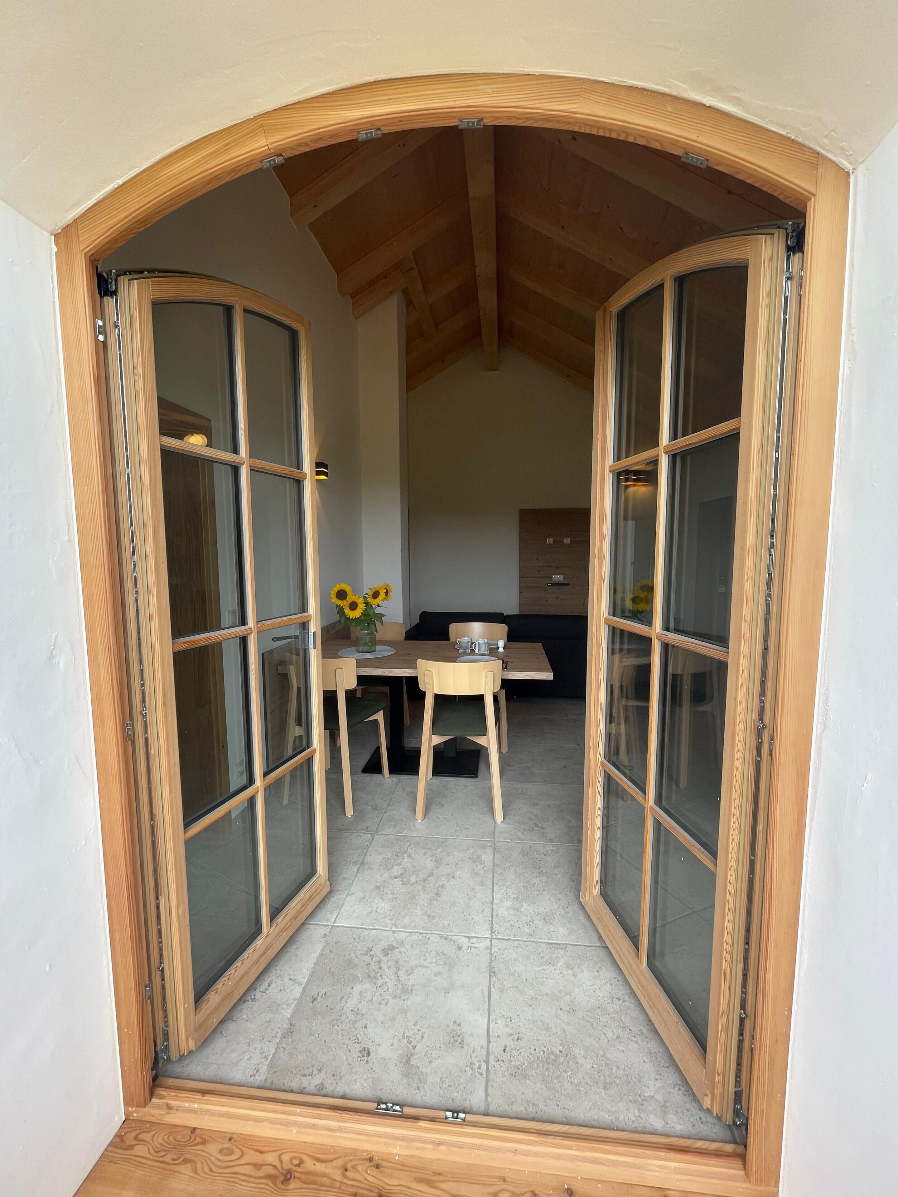 Une pièce dont la porte est encadrée de bois, et qui donne sur un coin repas avec une table, des chaises et un vase rempli de tournesols.