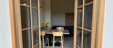 A room with a wooden-framed door leading to a dining area with a table, chairs, and a vase of sunflowers.