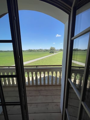 Blick vom Zimmer mit Balkon auf ein grünes Feld und einen klaren Himmel.