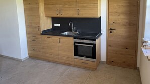 A compact kitchen with wooden cabinets, a black countertop, a built-in oven, and a stainless steel sink. - Bavasol – Your Temporary Bavarian Retreat (Schechen)