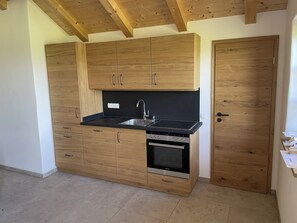 Eine kleine Küche mit Holzausstattung, einer schwarzen Arbeitsplatte, einem eingebauten Backofen und einer Spüle aus Edelstahl.