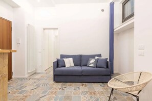 A room with a blue sofa, a wicker chair, patterned floor tiles, a white radiator, and a door. - Athens House • Near the Duomo [Loreto-Duomo] (Milano)