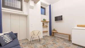 Un espai vital reduït amb un sofà, una cadira, un televisor penjat a la paret i un paviment amb dibuixos.