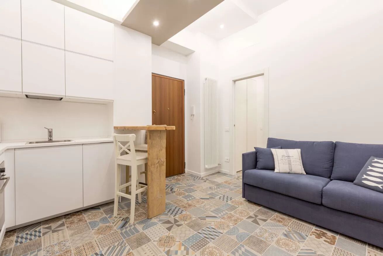 Een knus woongedeelte met een kitchenette, een bank en vloerbedekking met een patroon.