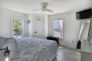 A bedroom with a bed, a ceiling fan, a dresser, a TV, and two windows. - Cheeky Crab A - 2 Bedroom Coastal Cottage Steps from the Beach (Garden City Beach)