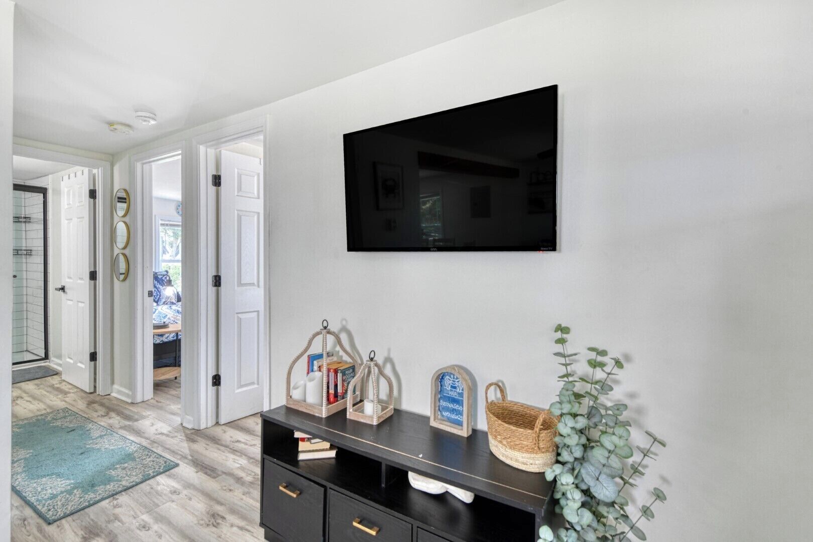 A hallway with a black console table, a mounted TV, and a door leading to another room.