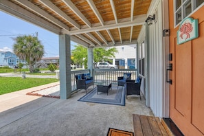 A covered porch with outdoor furniture, a concrete floor, and a view of the street. - Cheeky Crab B - 2 Bedroom Coastal Cottage Steps from the Beach (Garden City Beach)
