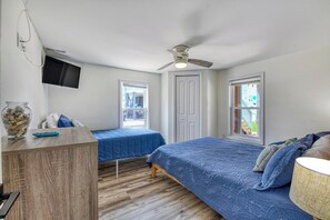 Ein Schlafzimmer mit zwei Betten, einem Deckenventilator, einem an der Wand montierten Fernseher und einem Fenster mit Jalousien.