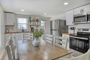 Uma cozinha moderna com armários brancos, uma mesa de jantar de madeira e um vaso central com flores.
