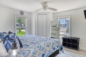 A bedroom with a bed, a ceiling fan, a door, and a window. - Cheeky Crab B - 2 Bedroom Coastal Cottage Steps from the Beach (Garden City Beach)