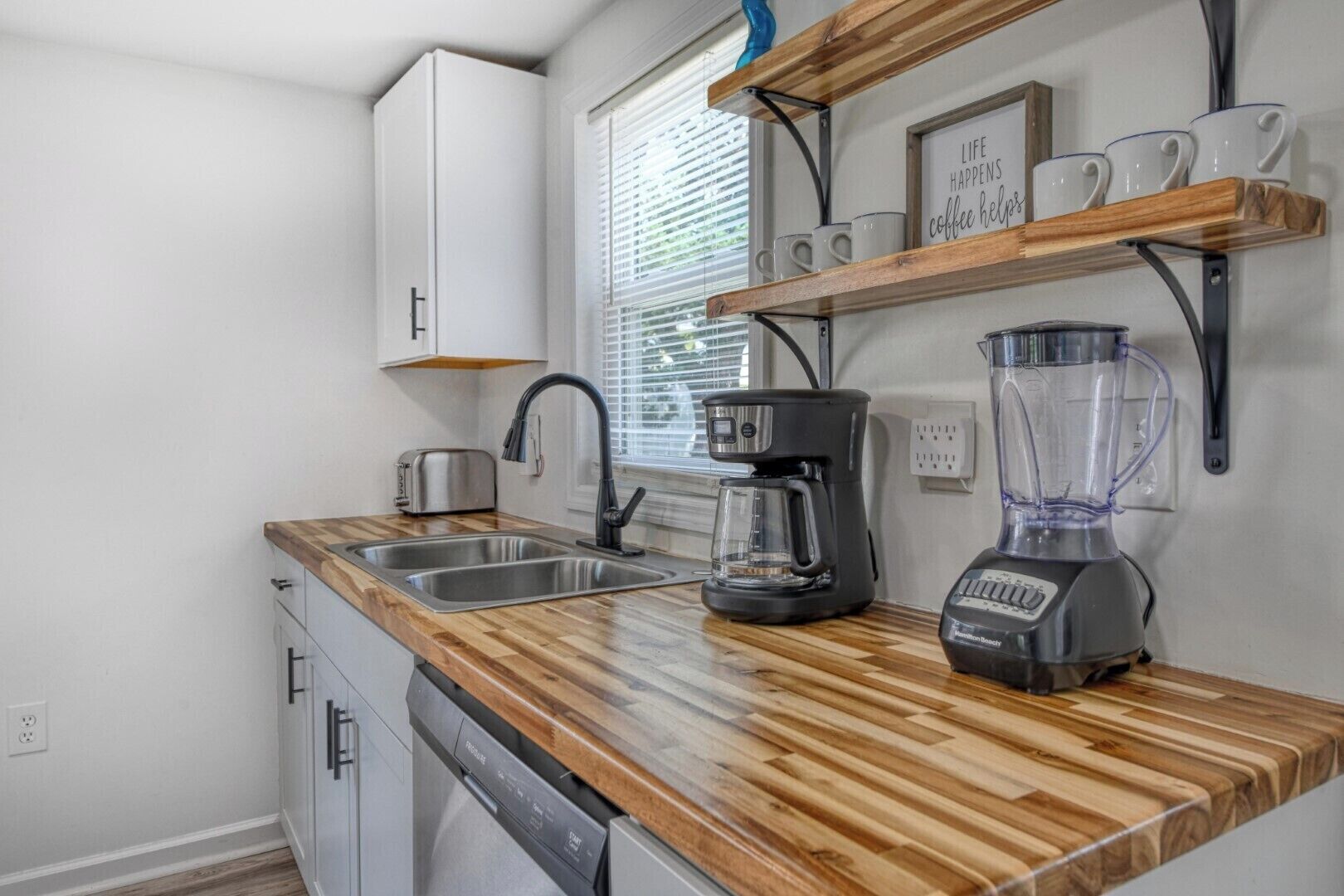 A kitchen with a wooden countertop, a coffee maker, a blender, a toaster, and a window with blinds.