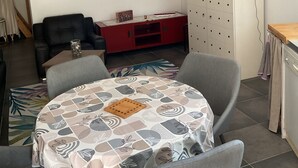 Olohuoneessa on ruokapöytä, harmaat tuolit, punainen mediakeskus, televisio ja taideteoksia seinillä.
