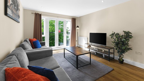 Uma sala de estar moderna com um sofá cinzento, uma mesa de centro, uma televisão e um vaso com planta.