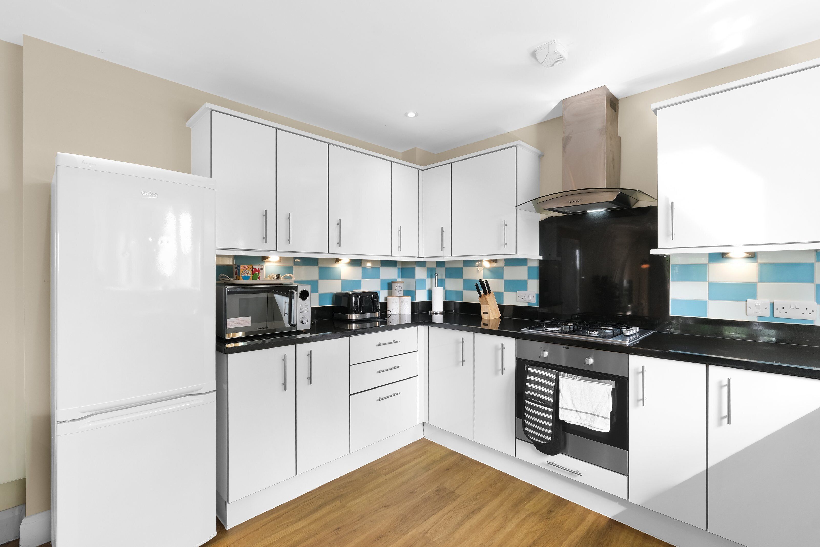 A modern kitchen with white cabinets, a black countertop, and a stainless steel range hood.