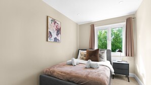 Um quarto com cama, mesa de cabeceira, janela e um quadro na parede.