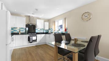A modern kitchen with white cabinets, a glass dining table, and a wall clock.