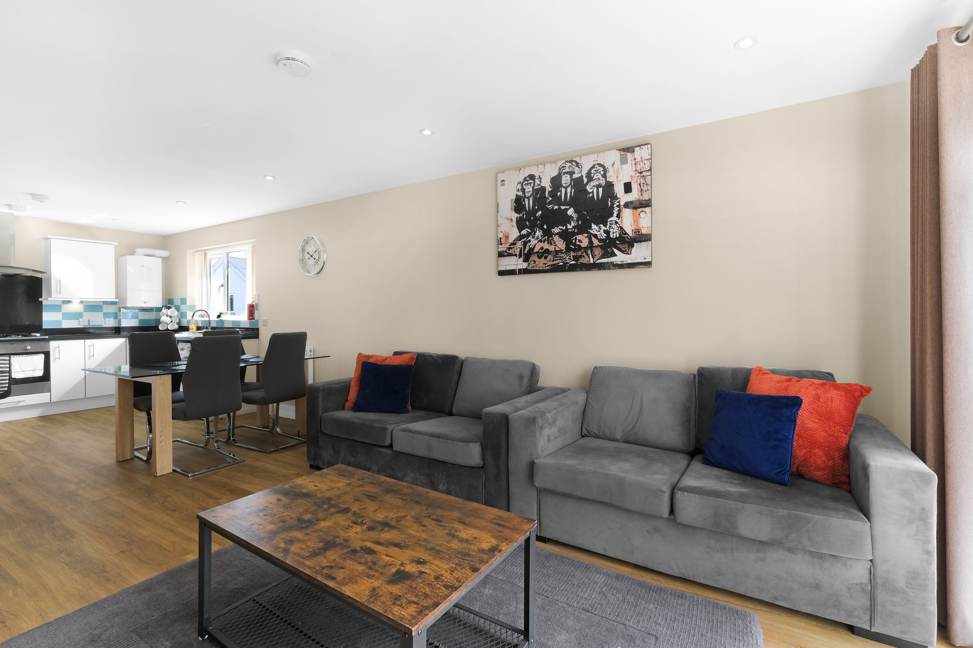 Uma sala de estar moderna com um sofá cinza, uma mesa de centro de madeira e um espaço de refeições com uma mesa e cadeiras de vidro.