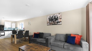Uma sala de estar moderna com um sofá cinza, uma mesa de centro de madeira e um espaço de refeições com uma mesa e cadeiras de vidro.
