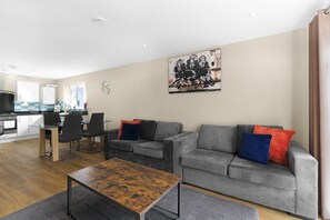 Ein modernes Wohnzimmer mit einem grauen Sofa, einem Holztisch und einem Essbereich mit einem Glastisch und Stühlen.