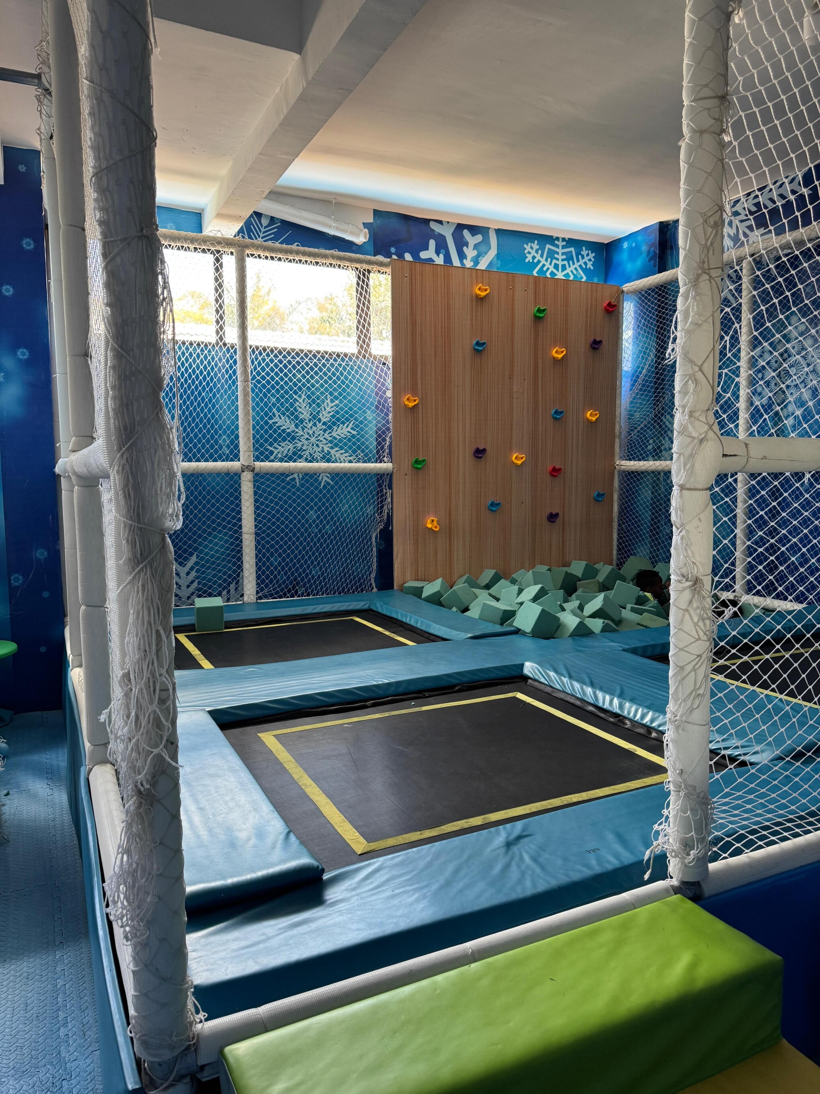 Un espace de jeux intérieur comprenant deux trampolines, des blocs de mousse rembourrés et un mur d’escalade.