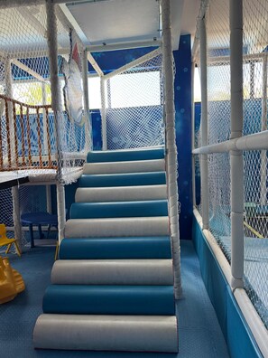 A multi-level indoor play area with netted walls and padded steps.