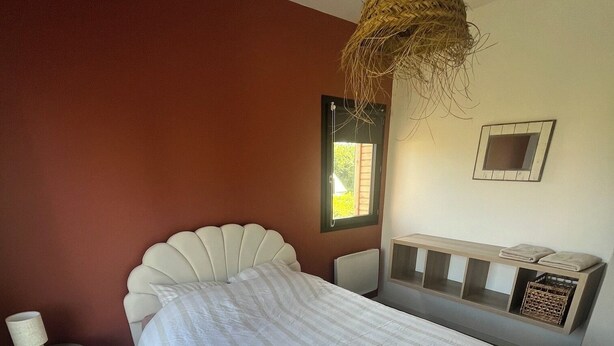 A bedroom with a bed, a nightstand, a lamp, a window, and a wall-mounted shelf. - BELLEVUE COTTAGE (Tréveneuc)