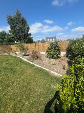 A well-maintained backyard with a lawn, a wooden fence, and various shrubs. - BELLEVUE COTTAGE (Tréveneuc)