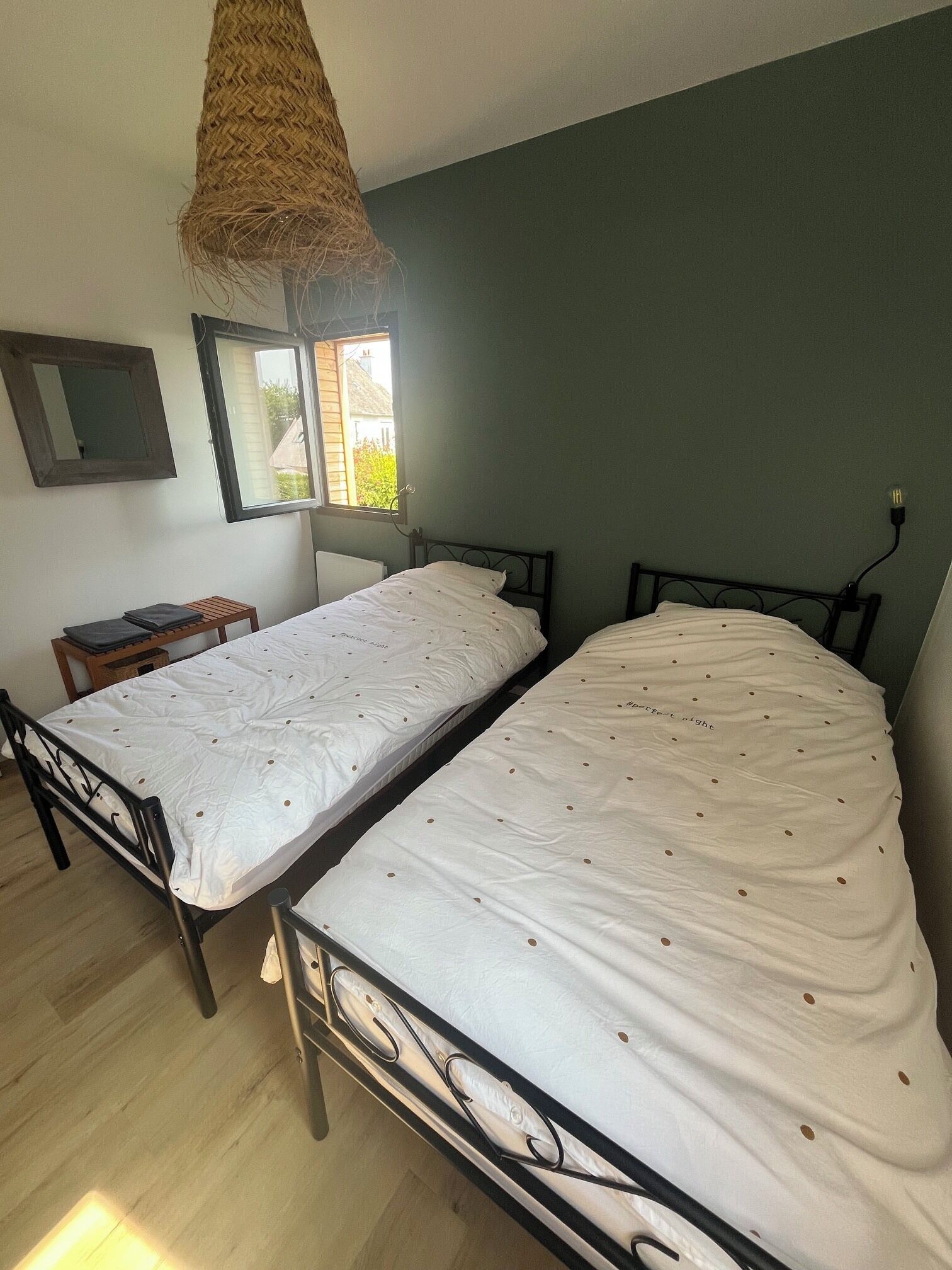 Ein Zimmer mit zwei Einzelbetten, einem kleinen Tisch, einer Hängeleuchte und einem Fenster mit Blick auf ein Haus.