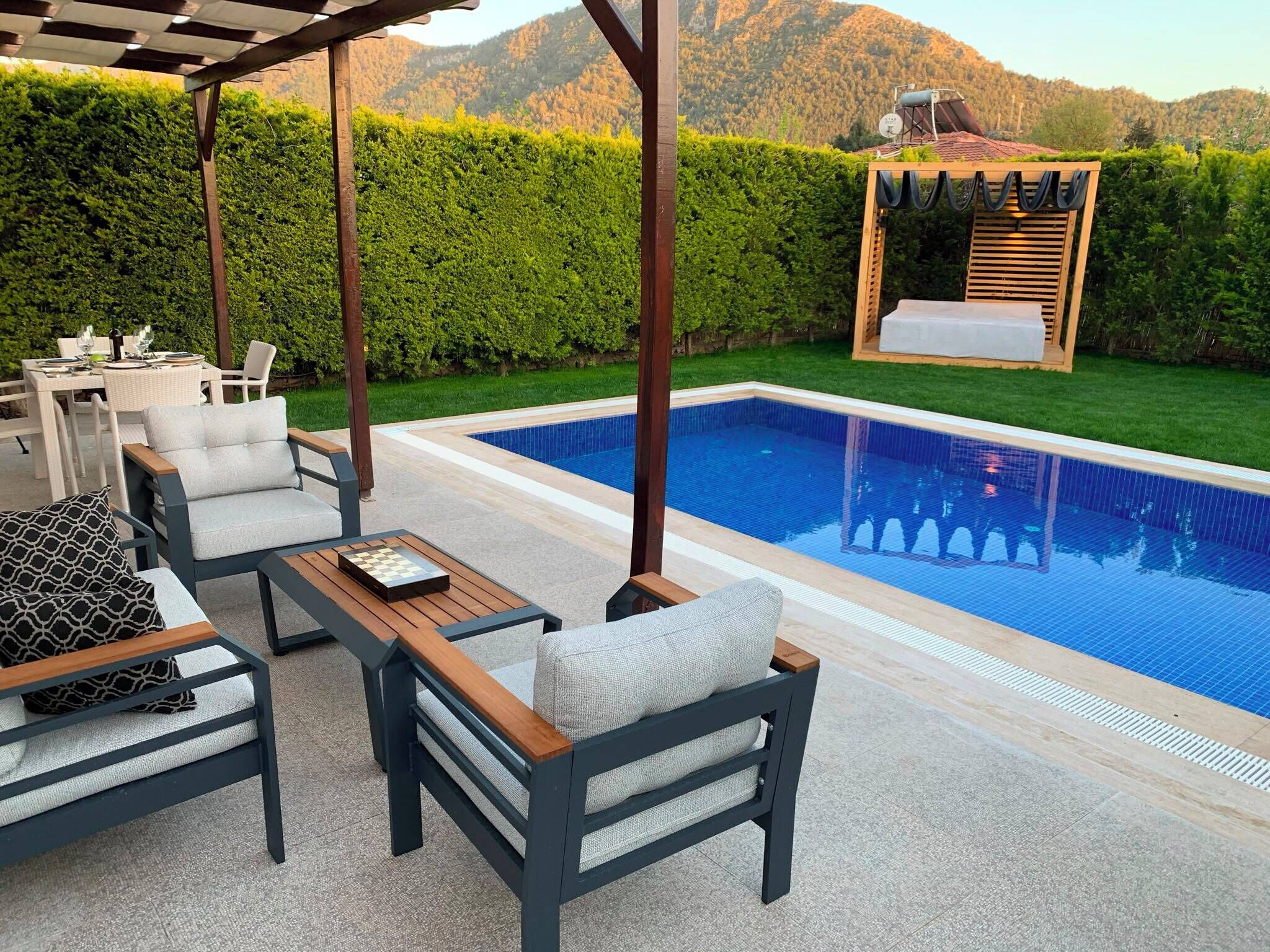A poolside area with outdoor furniture, a pergola, and a view of mountains.