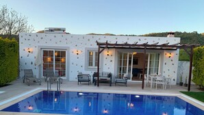 Een zwembadgedeelte met een pergola, zitplaatsen en uitzicht op een huis met stenen details.