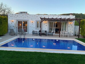 A poolside area with a pergola, seating, and a view of a house with stone accents. - Villa Vista (fethiye)