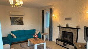 Een woonkamer met een blauwgroene bank, een houten salontafel, een open haard en een televisie.