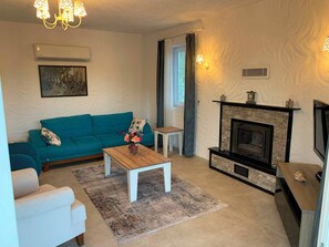 A living room with a teal sofa, a wooden coffee table, a fireplace, and a television. - Villa Vista (fethiye)
