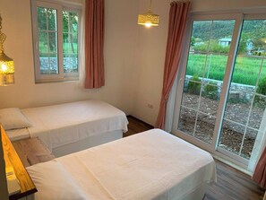 A bedroom with two beds, a window with curtains, and a hanging light fixture. - Villa Vista (fethiye)