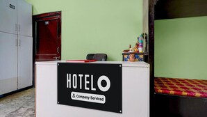 A hotel reception desk with a sign indicating it is company-serviced. There is a red door and a bed with a patterned bedspread in the background. - Hotel O Singar Nagar Metro Station Lucknow (Lucknow)