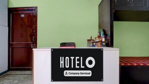 A hotel reception desk with a sign indicating it is company-serviced. There is a wooden door and a bunk bed in the background. - Hotel O Singar Nagar Metro Station Lucknow (Lucknow)