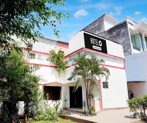 A hotel with a sign indicating it is company-serviced, a white facade with red accents, and a small garden area with potted plants. - Hotel O Singar Nagar Metro Station Lucknow (Lucknow)