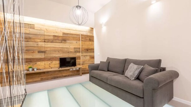 Ein modernes Wohnzimmer mit grauem Sofa, einer Holzwandverkleidung mit Flachbildfernseher und einer Hängeleuchte.