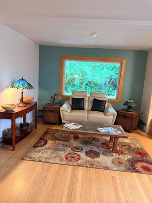 A living room with a sofa, coffee table, and a large window with a view of trees. - Family-Ready Downtown Cedar Cottage (Fairbanks)