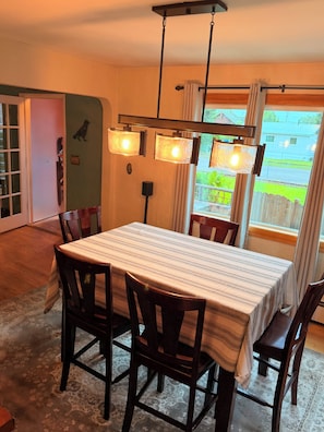 A dining area with a table and chairs, a hanging light fixture, and a view of the outdoors. - Family-Ready Downtown Cedar Cottage (Fairbanks)