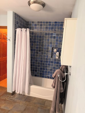 A bathroom with a bathtub, a shower curtain, a towel rack, and a tiled wall. - Family-Ready Downtown Cedar Cottage (Fairbanks)