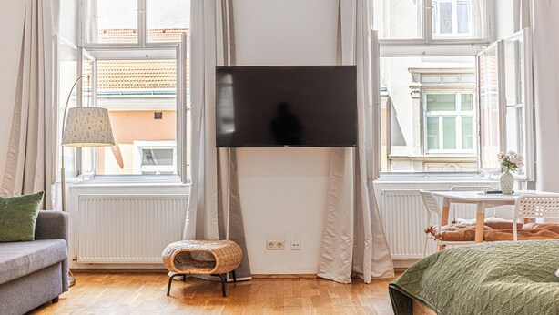 Une pièce avec un grand téléviseur fixé au mur, un canapé, une petite table avec un vase et une chaise.