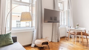 Une pièce comprenant un canapé, une petite table avec des chaises, un lampadaire et un téléviseur fixé au mur.