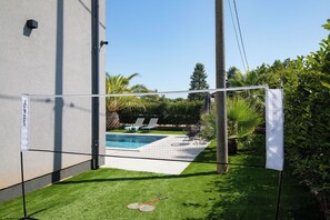 Ein Garten mit Pool, Tennisnetz und einer kleinen Rasenfläche.
