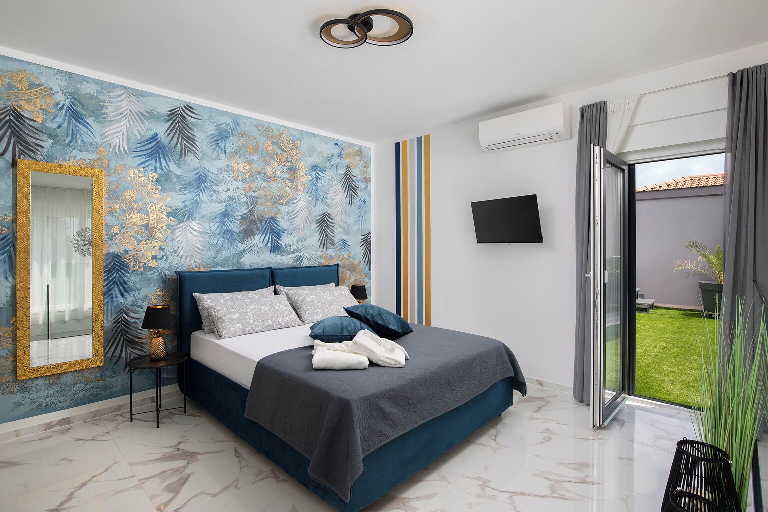 Une chambre moderne avec un grand lit, un miroir, un téléviseur à écran plat et une vue sur une pelouse verdoyante.