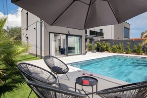 Ein moderner Poolbereich im Freien mit Glastür, Liegestühlen und einem Tisch mit Gläsern.