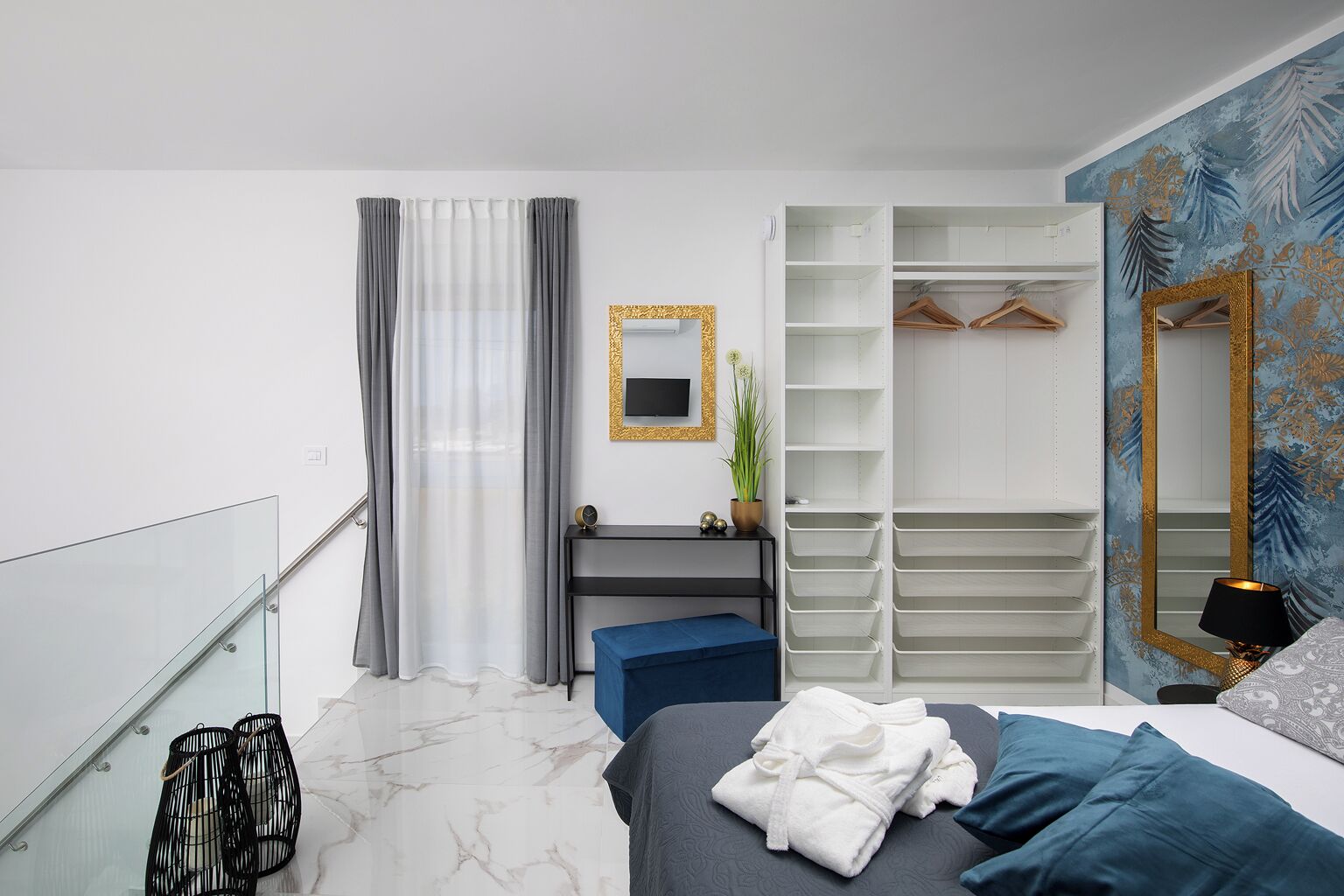 A modern bedroom with a bed, bedside table, mirror, wardrobe, and a view of the outside.